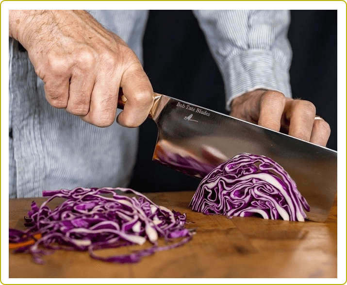 A person slicing red cabbage on top of a wooden table.